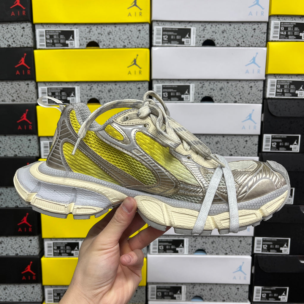 Balenciaga unisex sneakers angled view, metallic gray upper with yellow stripe and laces