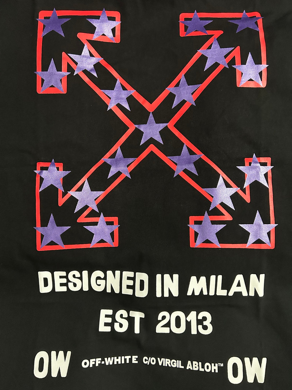 Black T-shirt graphic close-up with red frame, purple stars, and 'DESIGNED IN MILAN'