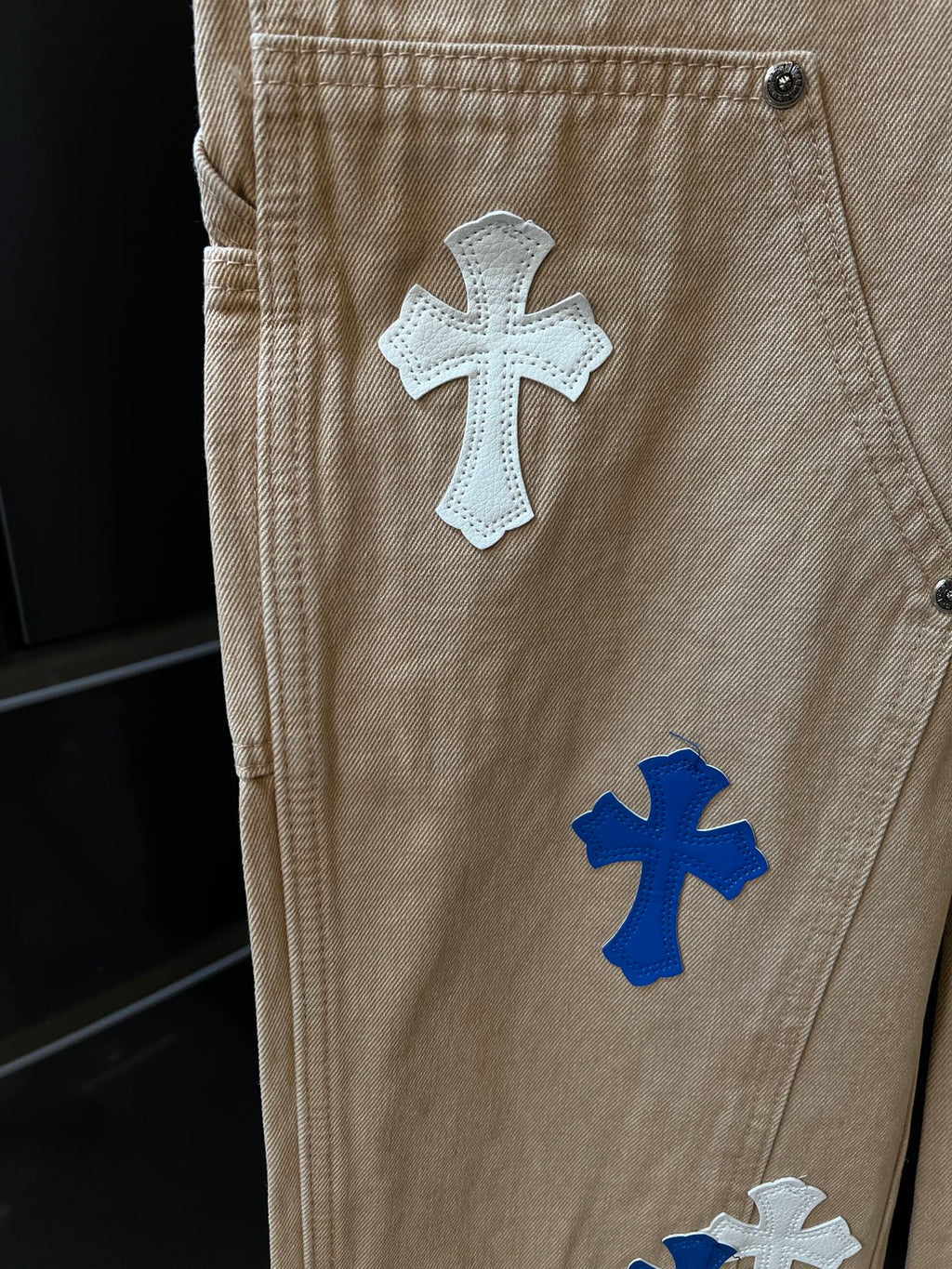 Beige denim pants with embroidered cross patches on back panel and pockets