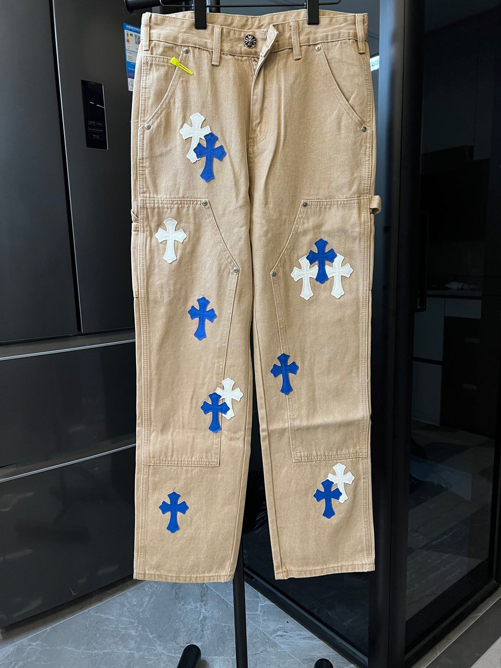 Khaki work pants with blue and white cross patches, zip fly and belt loops