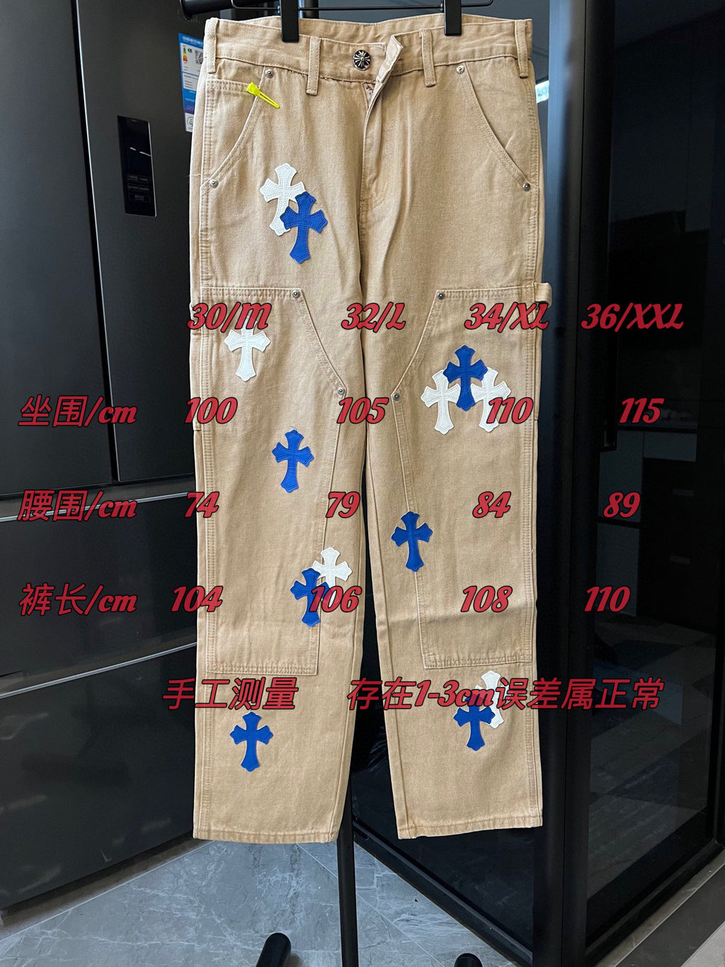 Beige denim cargo pants with embroidered cross patches and size labels visible