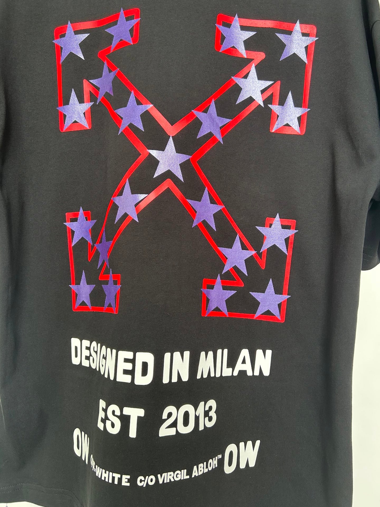 Off-White dark T-shirt with large star emblem and white text: “DESIGNED IN MILAN EST 2013”.