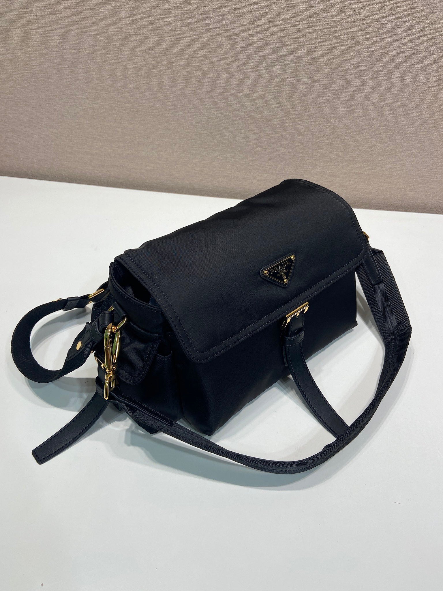 Prada crossbody bag, dark navy, side view with flap, strap, and gold zipper pulls