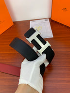 Leather belt with dark textured strap and gold-toned H buckle in hand