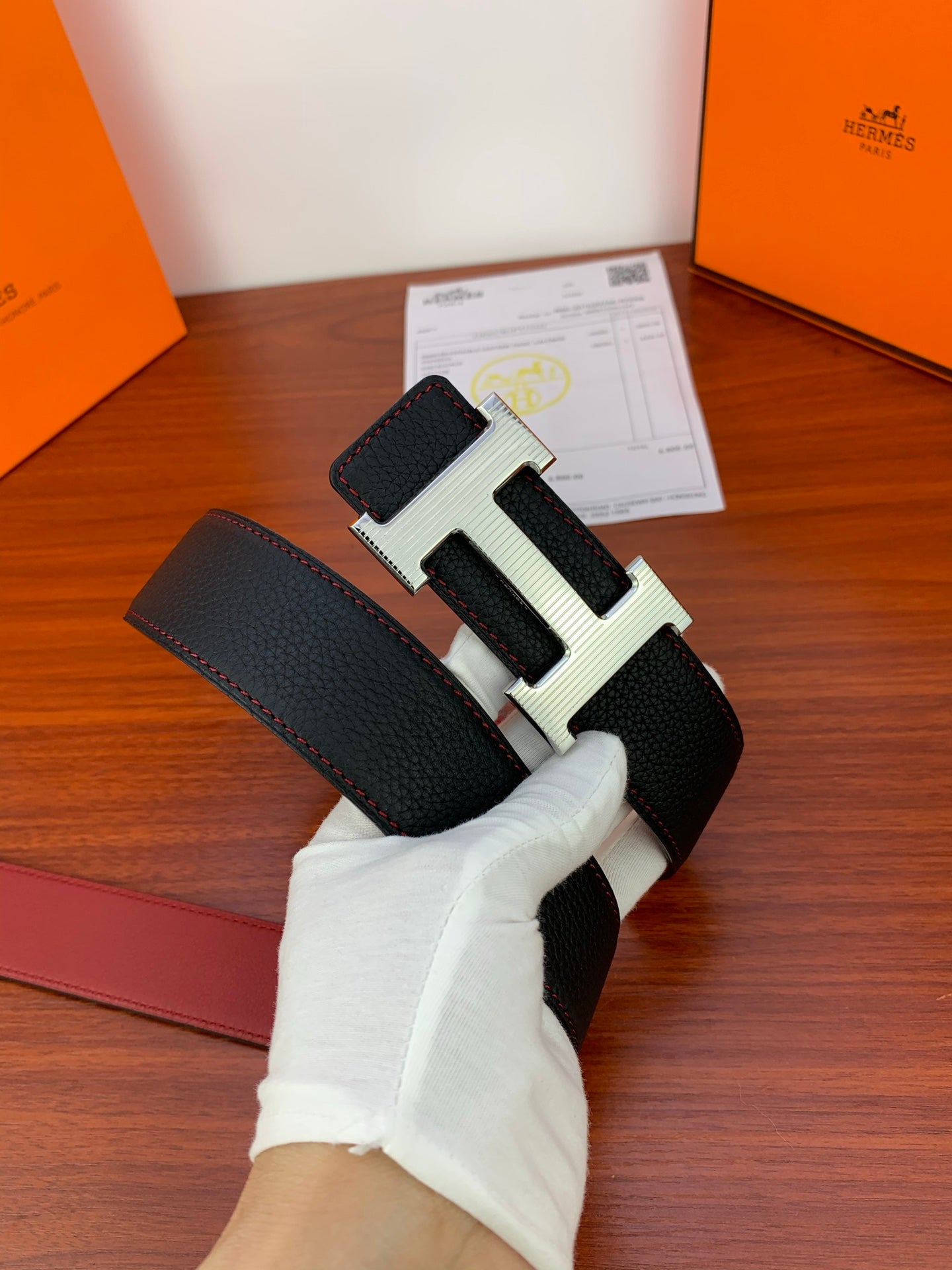 Leather belt with dark textured strap and gold-toned H buckle in hand