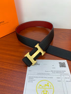 Dark leather belt with gold H buckle and red underside on the reversible strap