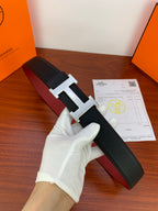 Hermes belt with black textured strap and silver H buckle, held in white-gloved hand
