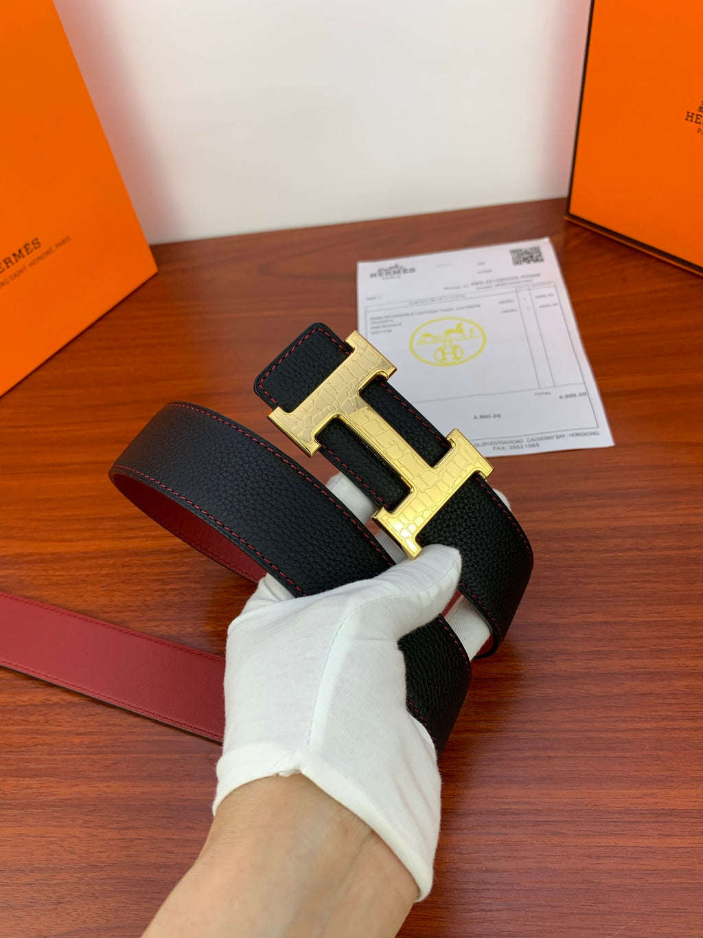 Hermes reversible belt with black strap and gold buckle, certificate papers on table