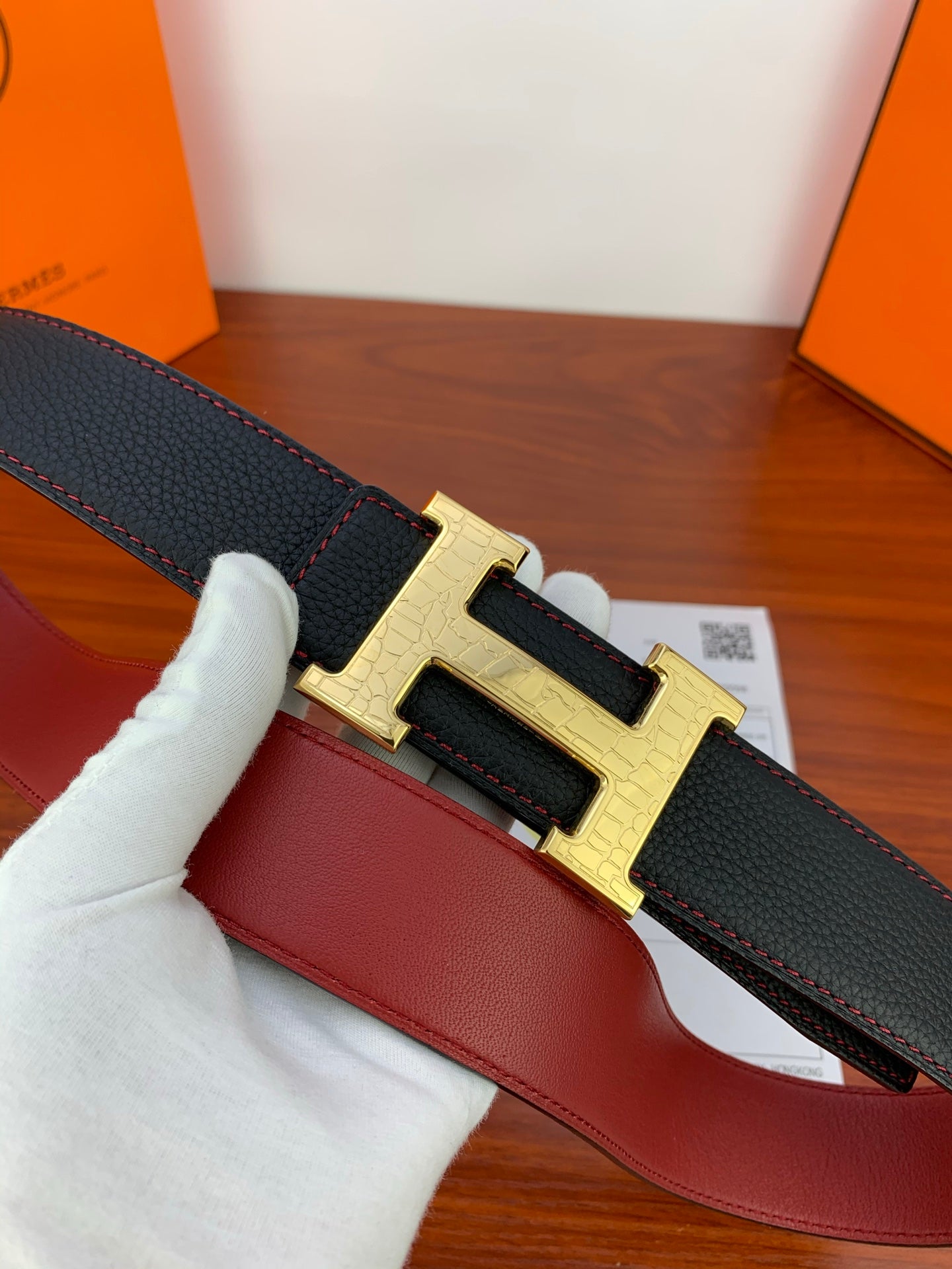 Hermes belt with black textured strap and gold buckle, close-up held by white glove