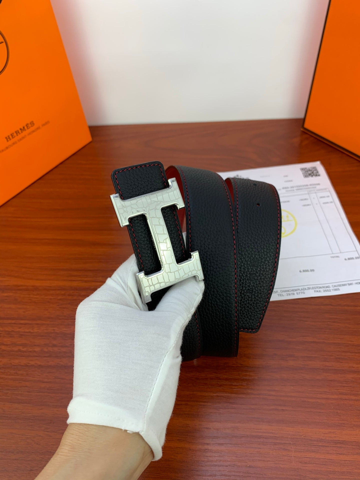 Hermes reversible belt with black outer and red underside, silver buckle shown in hand