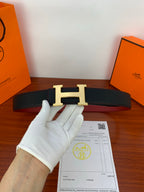 Hermes belt with black strap and gold H buckle, flat view with paperwork below