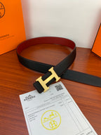 Black leather belt with gold H buckle, strap looped for a flat view.