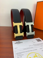 Black leather belt with H buckle, gold and silver finishes shown upright.