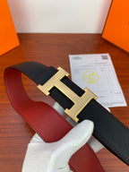 Reversible leather belt with black textured strap and gold-tone H buckle over red lining