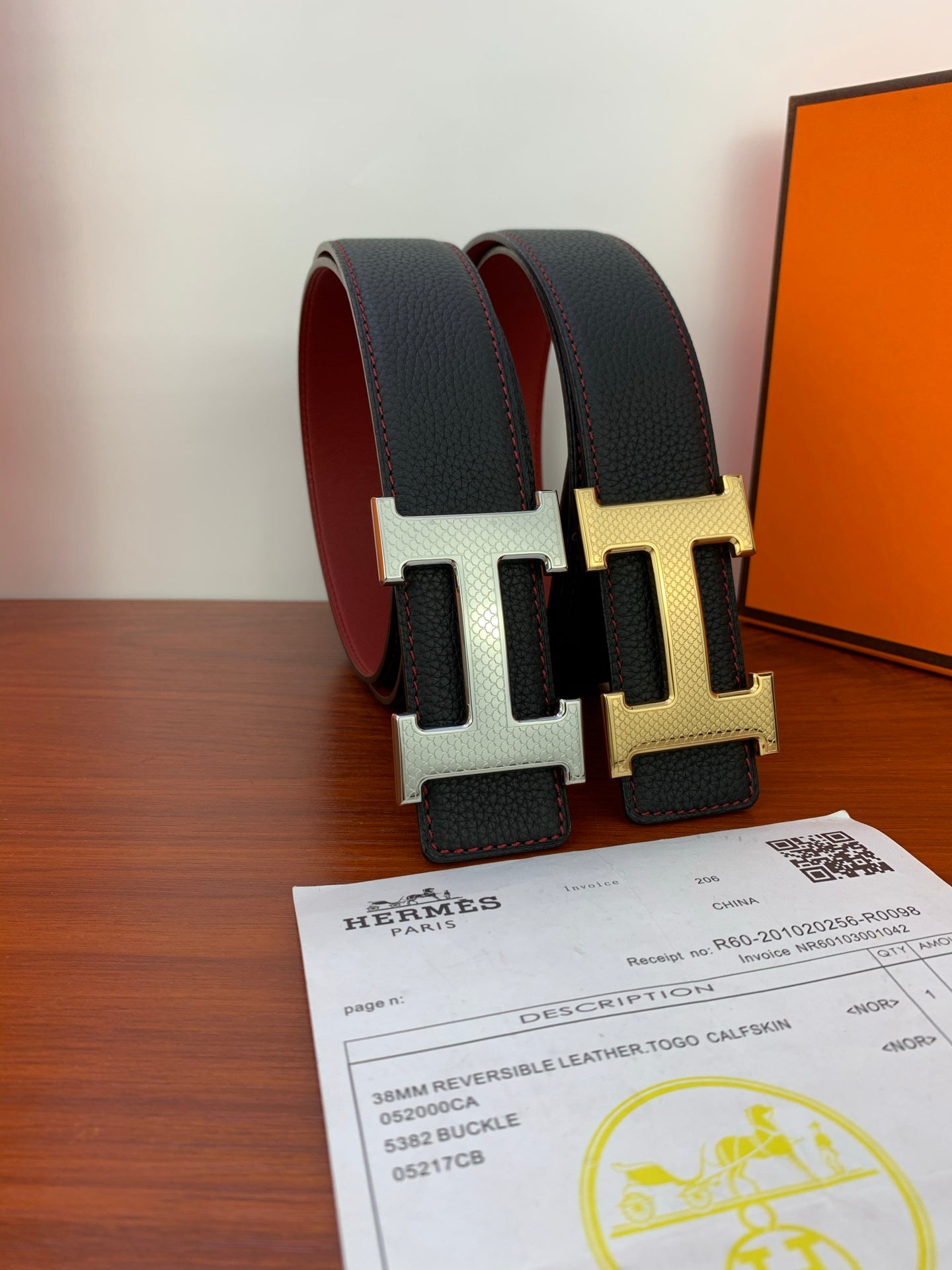 Reversible leather belt close-up with black straps and gold and silver H buckles
