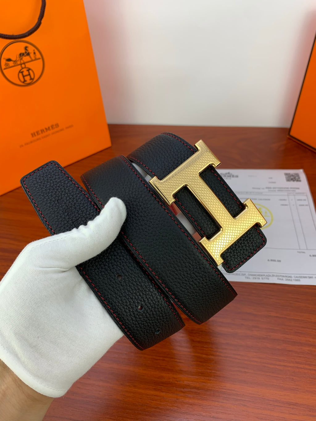 Reversible leather belt with black textured strap and gold-tone H buckle, close-up