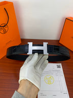 Hermes leather belt with light metal H buckle and dark textured strap, held up