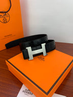 Hermes leather belt on an orange box: dark textured strap with light metal H buckle