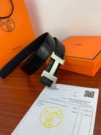Hermes leather belt with dark textured strap and light metal H buckle, angled view