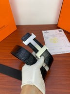 Hermes belt with dark textured leather and light metal H buckle, held above card