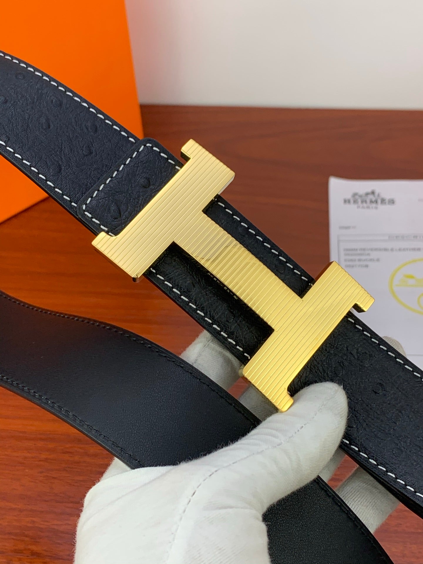 Hermes dark leather belt close-up, gold ribbed H buckle, contrast stitching