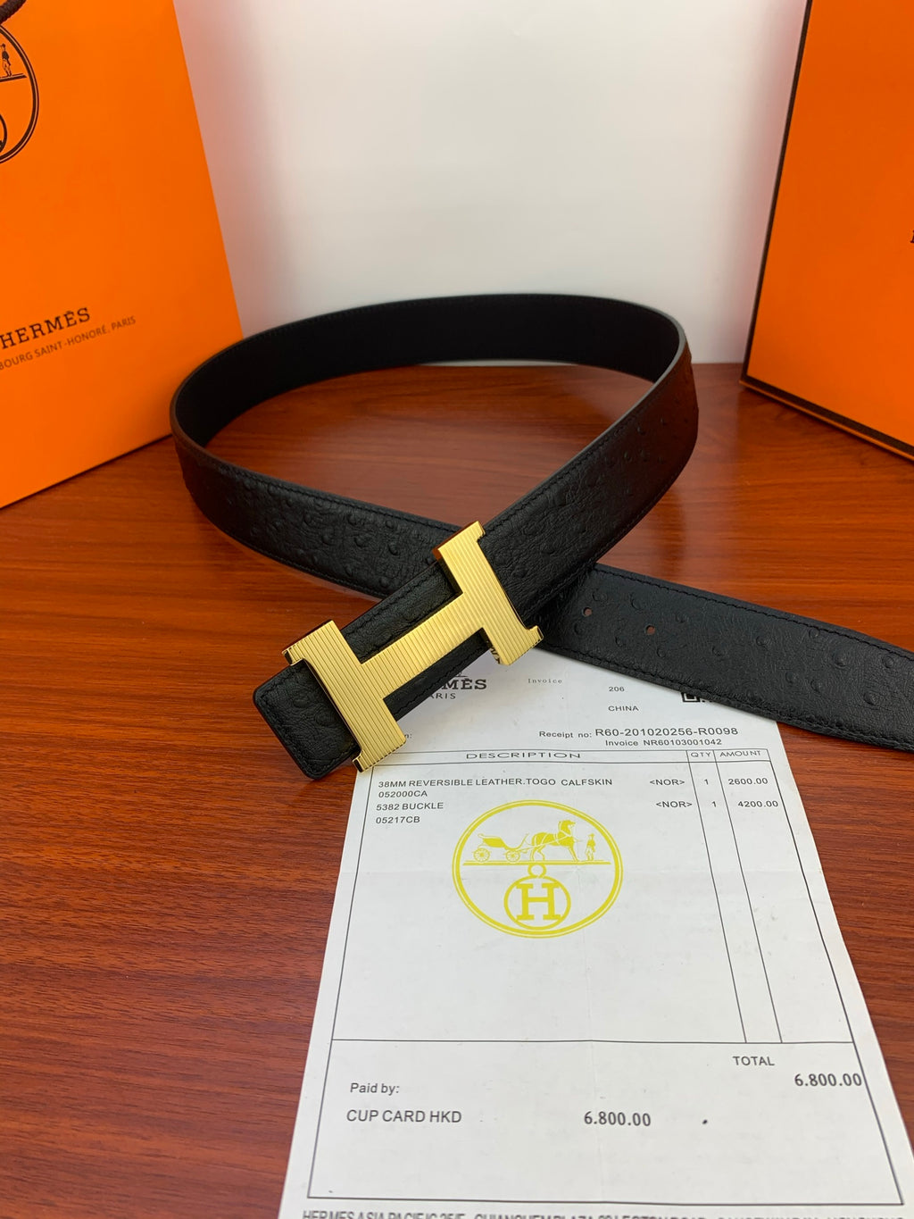Black leather belt with gold H buckle on top of paperwork