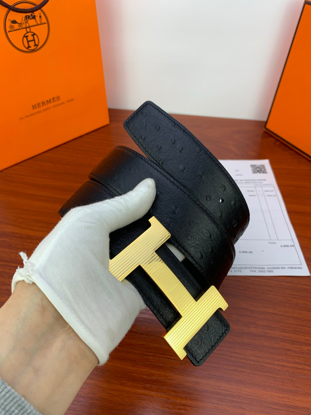 Black leather belt with gold H buckle, shown from side in gloved hand