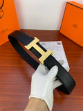 Black leather belt with gold H buckle, held in gloved hand