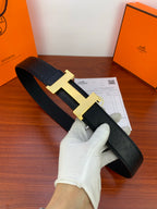 Black leather belt with gold H buckle, held in gloved hand