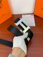 Black leather belt with gold H buckle, photographed at an angle in gloved hand
