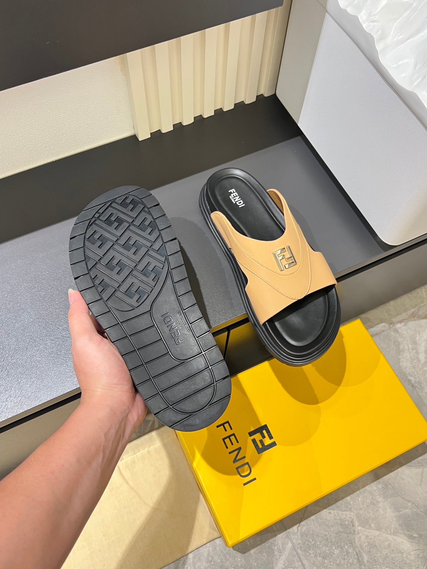 Fendi tan slide sandal outsole with textured black tread, shown in hand