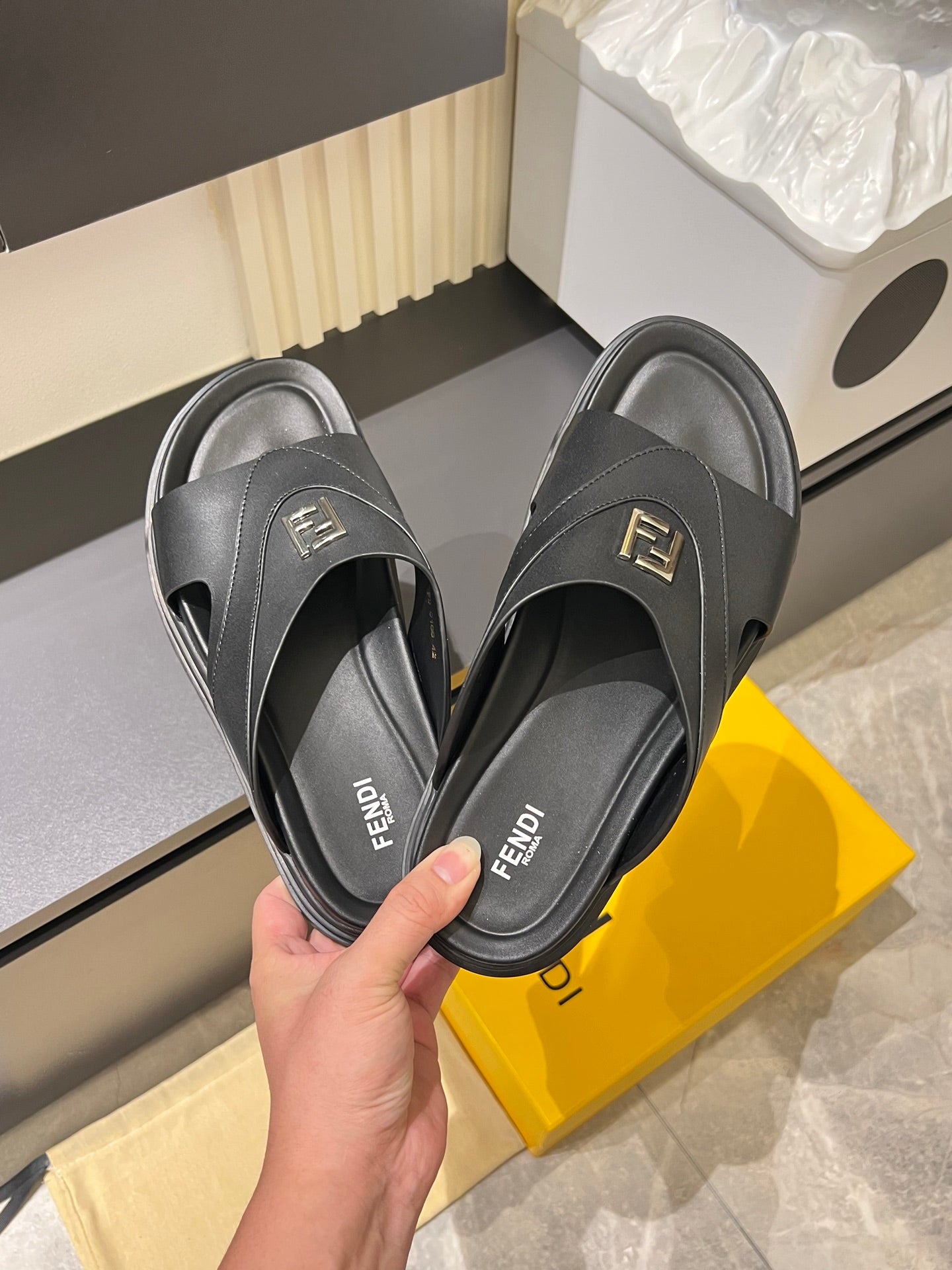 Fendi black slide sandals held in hand, FF logo on strap