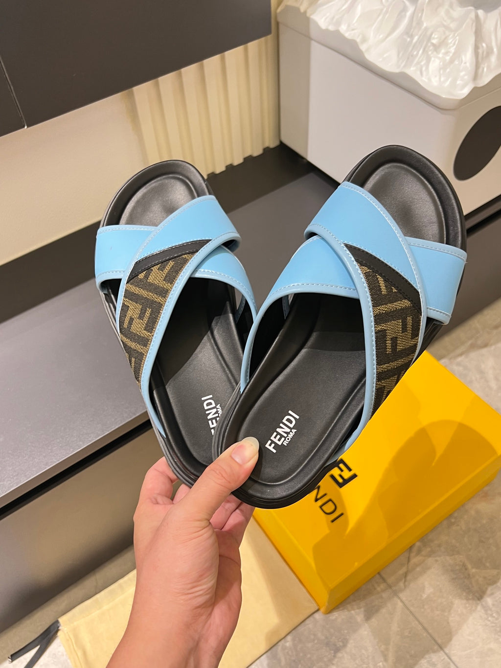 Fendi slide sandals with light blue straps over dark footbeds, held in hand