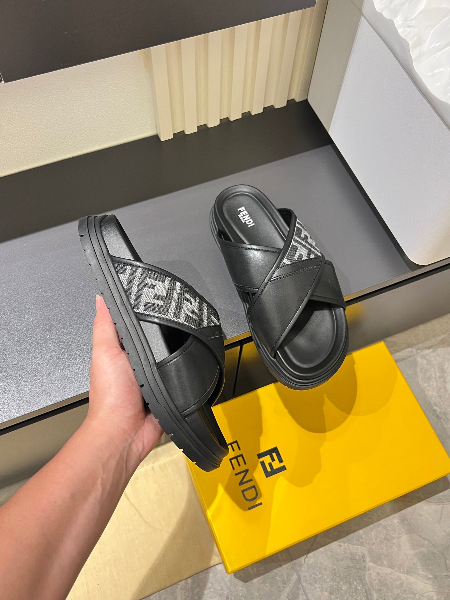 Black Fendi slide sandals with FF logo straps, held in a hand