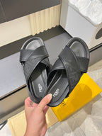 Fendi black slide sandals held in hand, crisscross straps and textured strap finish