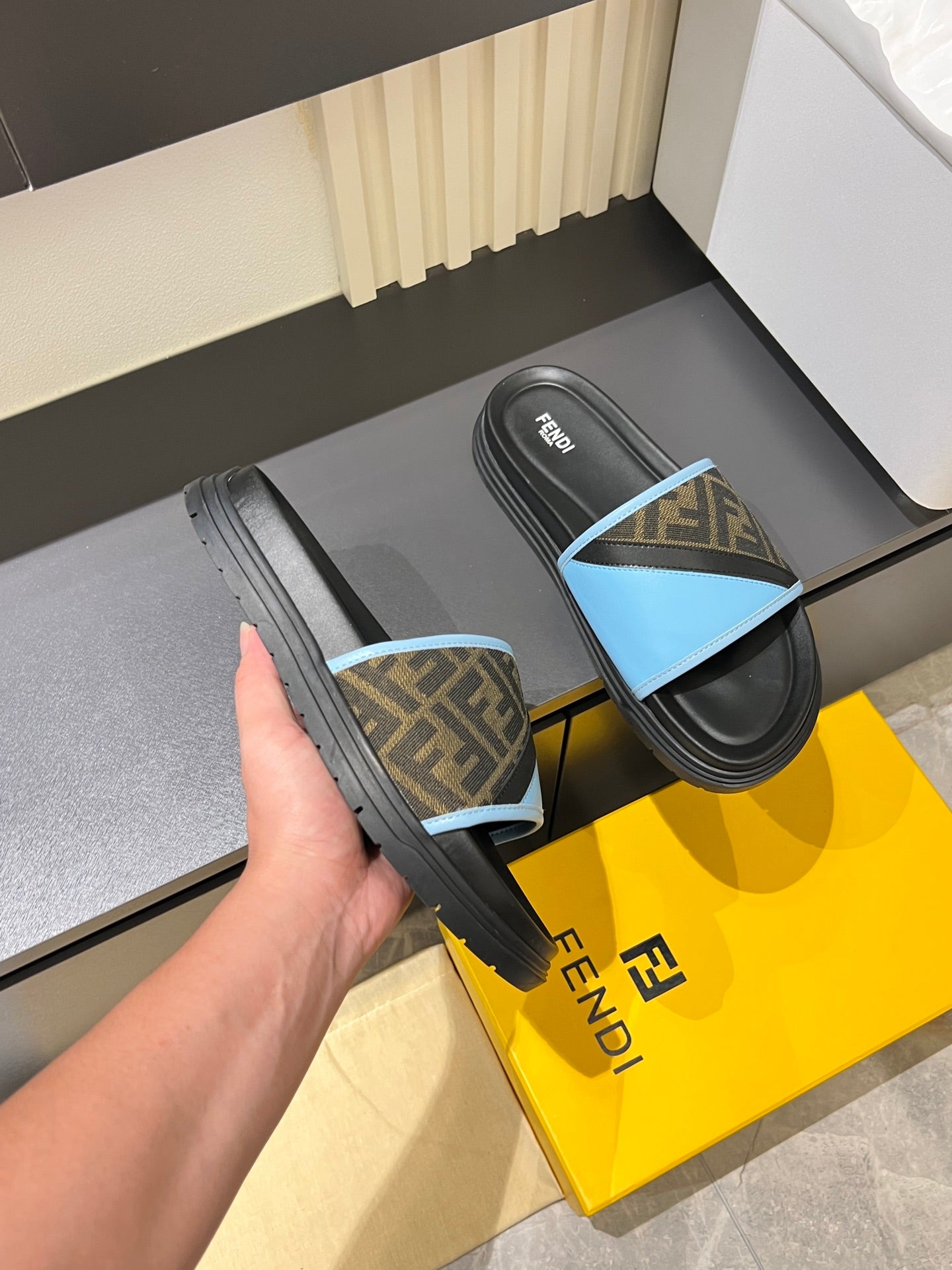 Fendi slide sandals held in hand; black sole with light blue FF strap