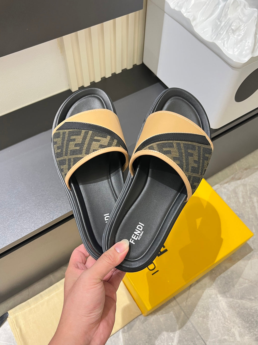 Fendi slide sandals in hand, black leather footbed with tan FF logo strap and trim