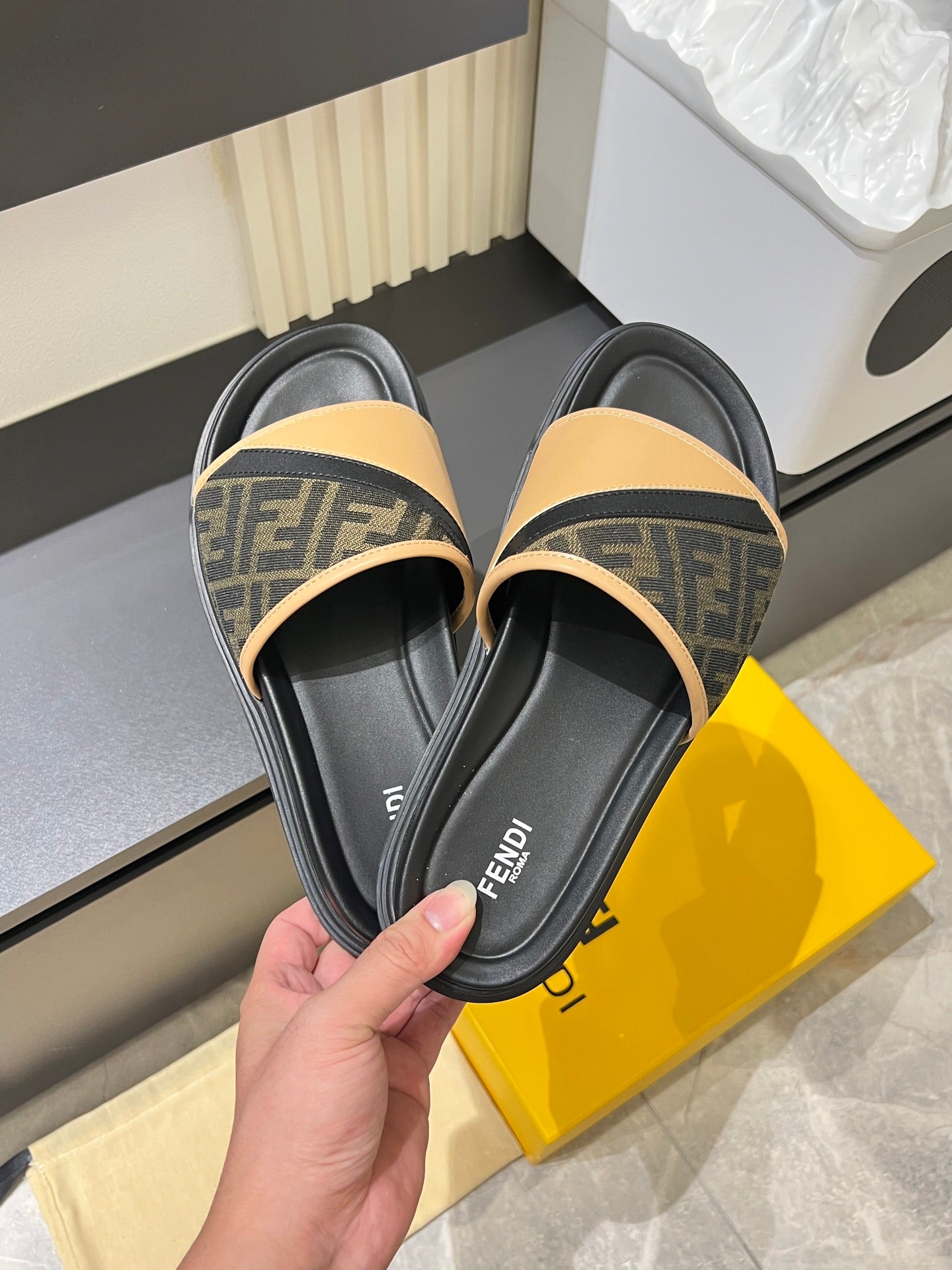 Fendi slide sandals in hand, black leather footbed with tan FF logo strap and trim