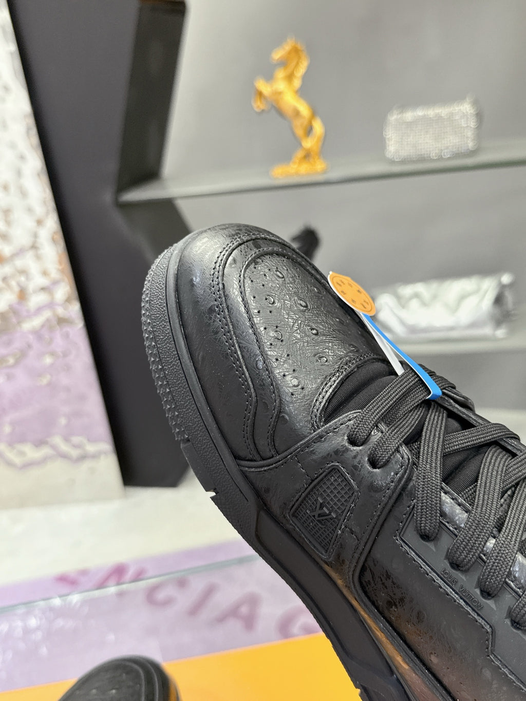 Black sneaker close-up with lace-up eyelets, embossed logo on side, and textured toe