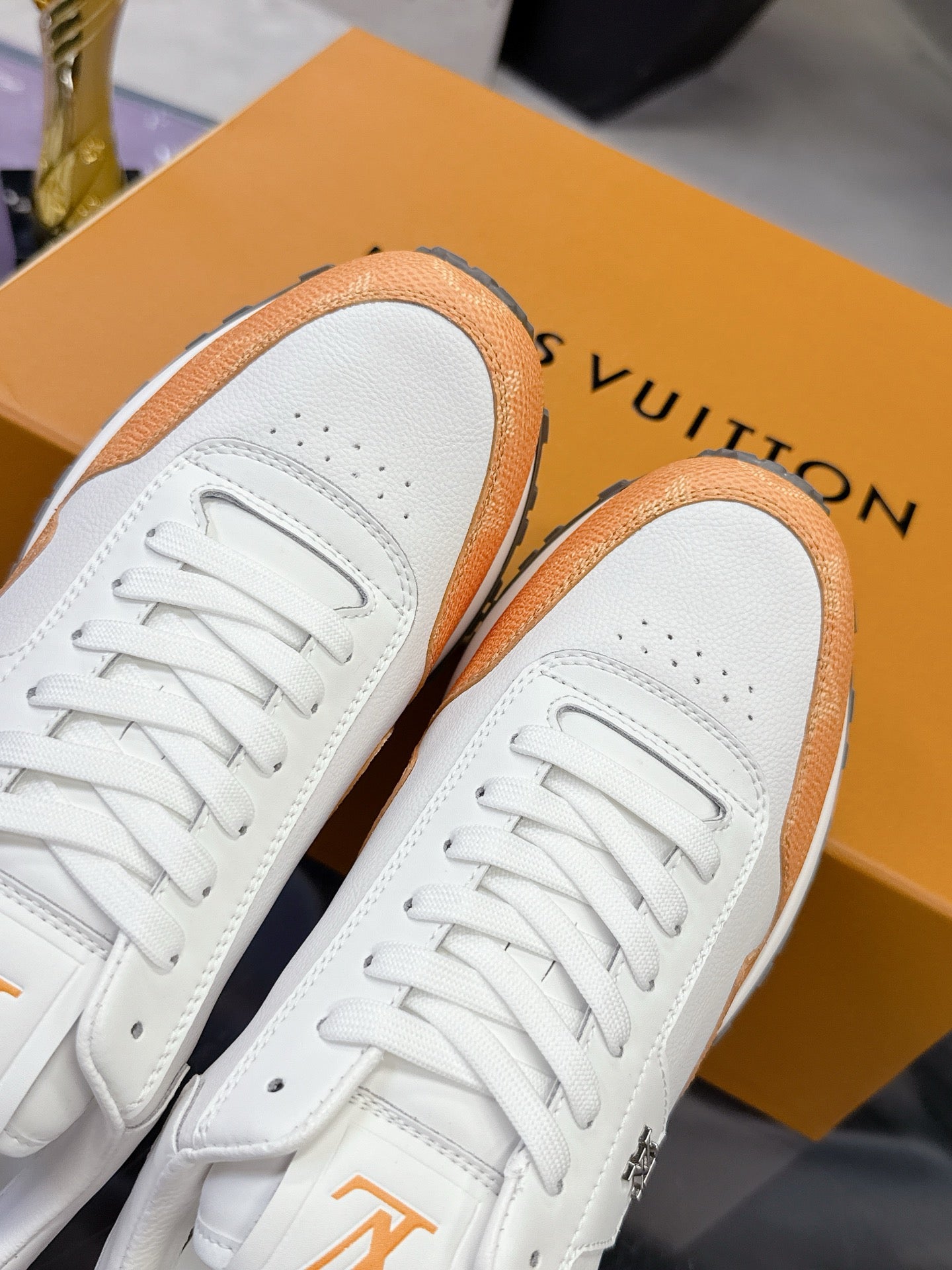 Close-up of white sneakers with orange trim, lace eyelets, and logo on side