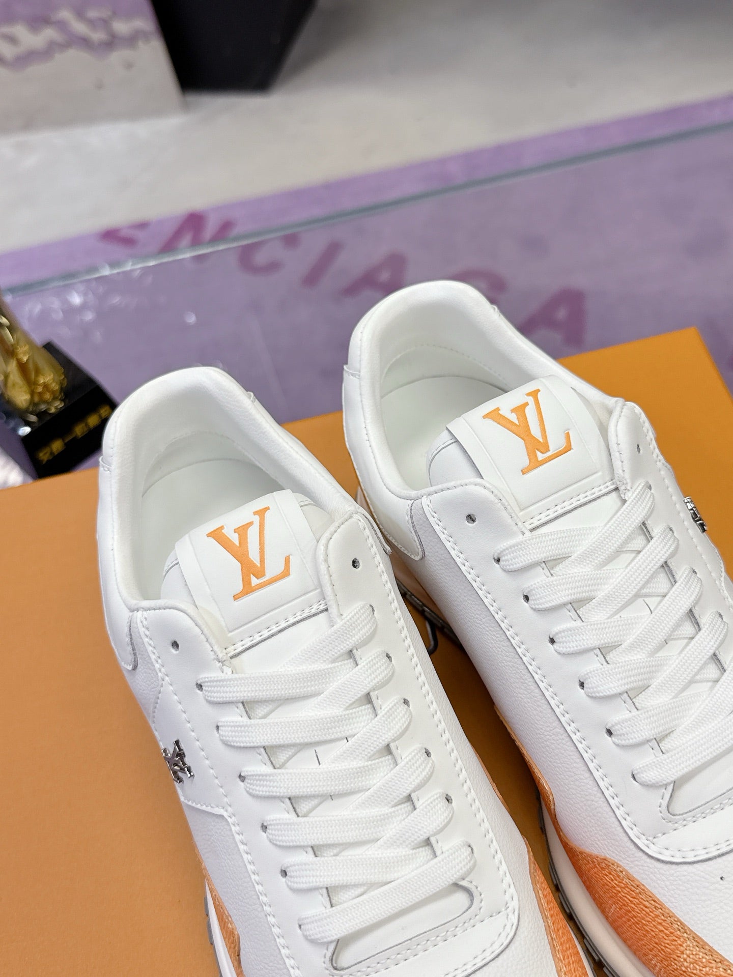 Close-up of white sneakers with orange trim and gold logo on the tongue