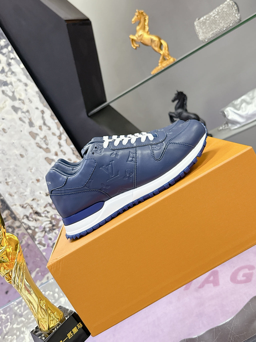 Blue leather low-top sneakers on orange box, embossed logo detail and white laces.