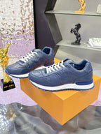 Blue leather low-top sneakers pair on orange box, white laces and rounded toe.