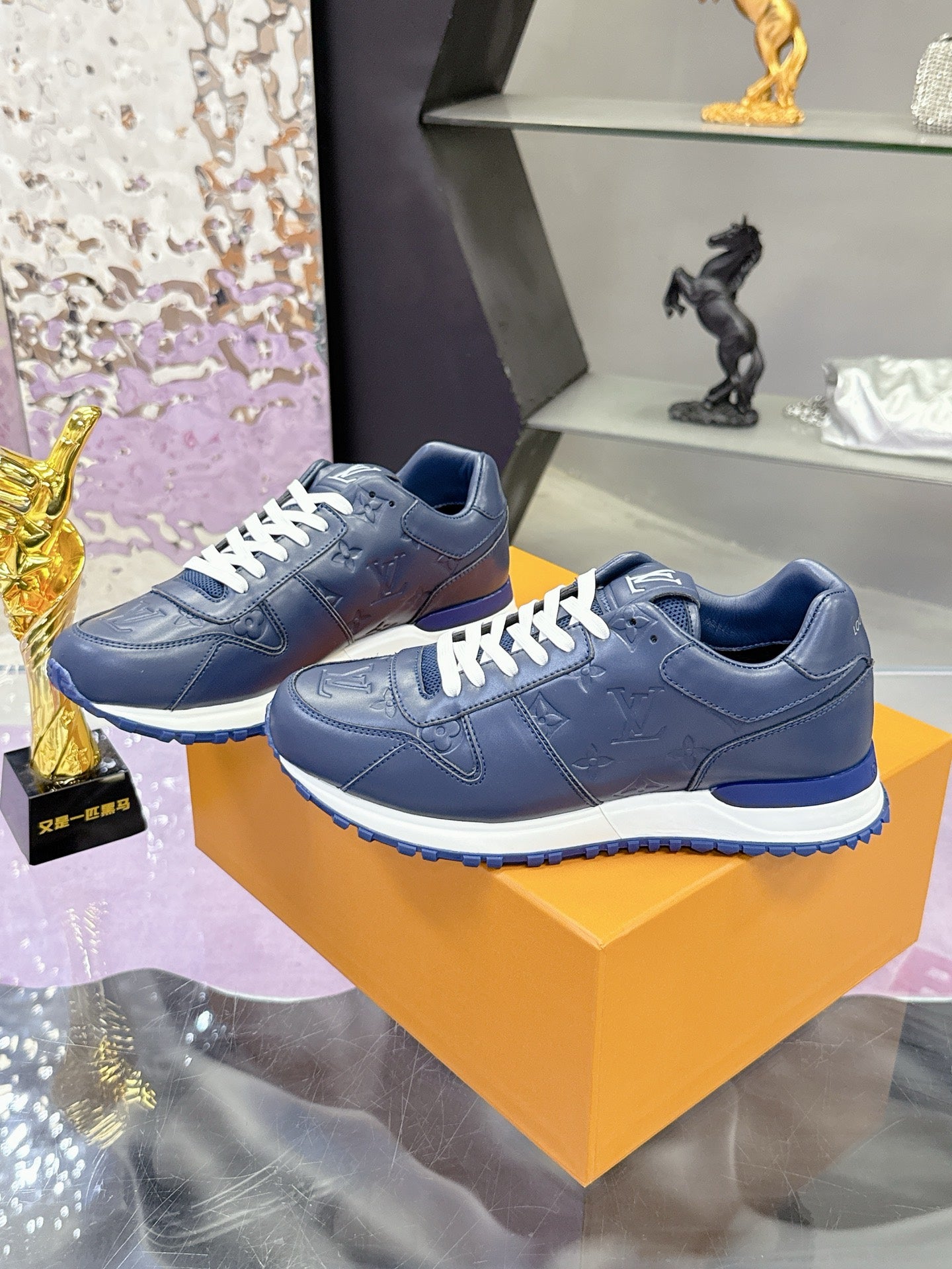 Blue leather low-top sneakers pair on orange box, white laces and rounded toe.