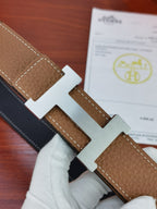 Reversible leather belt close-up: tan pebbled leather with gold H buckle, dark lining