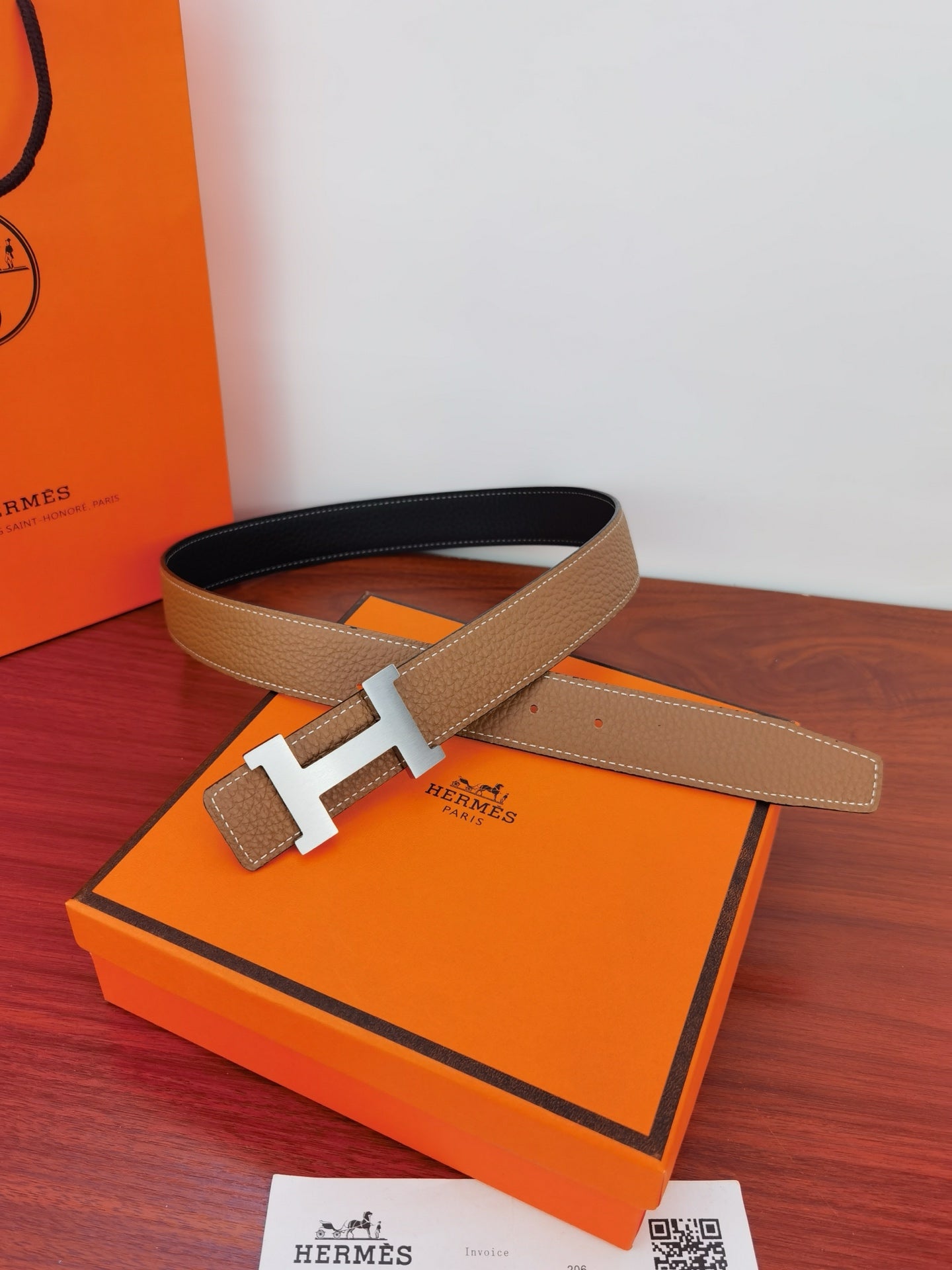 Reversible leather belt on orange box: tan pebbled strap with gold H buckle