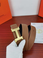 Reversible leather belt detail: tan pebbled straps with gold H buckle, dark strap behind