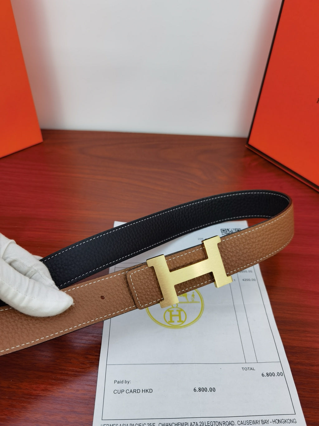 Reversible leather belt, tan front and dark back with gold H buckle, receipt beside