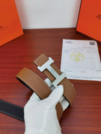 Reversible leather belt laid flat: tan leather with gold H buckle and dark underside