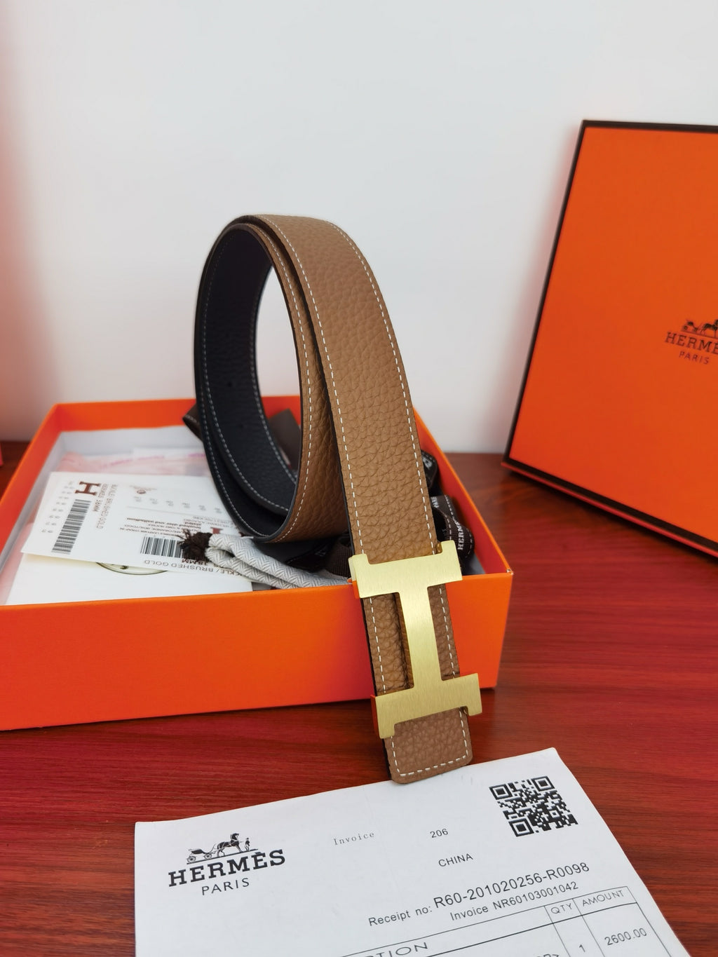 Reversible leather belt in orange box: tan strap loop with gold H buckle and dark underside